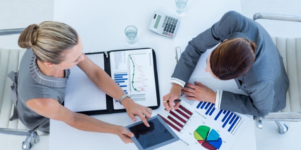 Two financial quantitative analysts sitting at a desk opposite of each other, looking at a chart, and evaluating investment opportunities.