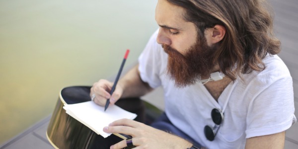 A lyricist writing lyrics on a piece of paper, using the back of his guitar to write on.