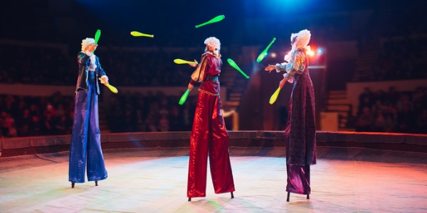 Three stilt walkers juggling at a circus performance.