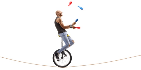 A juggler keeping several objects in the air while on a unicycle.