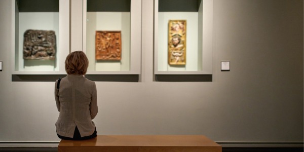 A woman sitting on a bench and looking at an exhibit that a curator was responsible for.